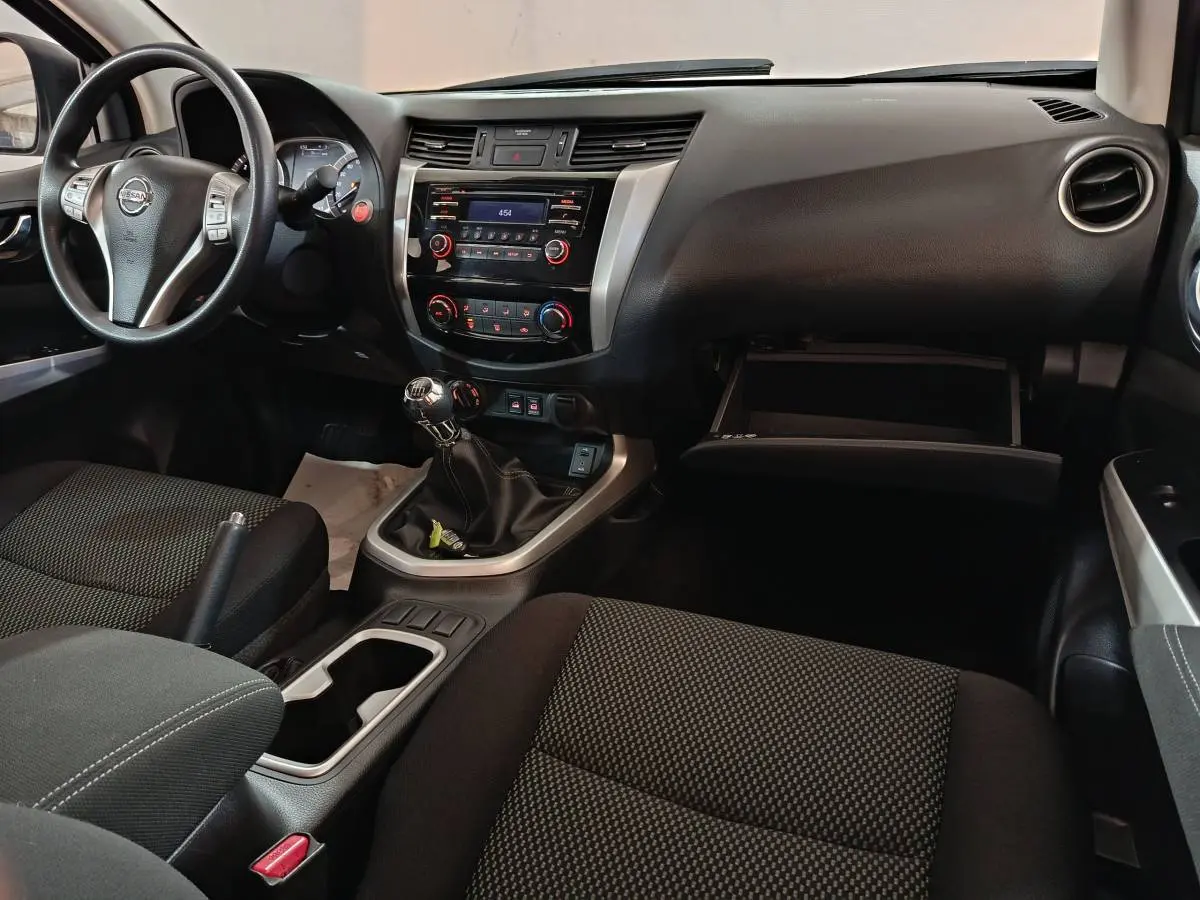 Vue intérieure côté conducteur du Nissan Navara 2018, montrant tableau de bord noir, volant multifonctions et boîte manuelle.