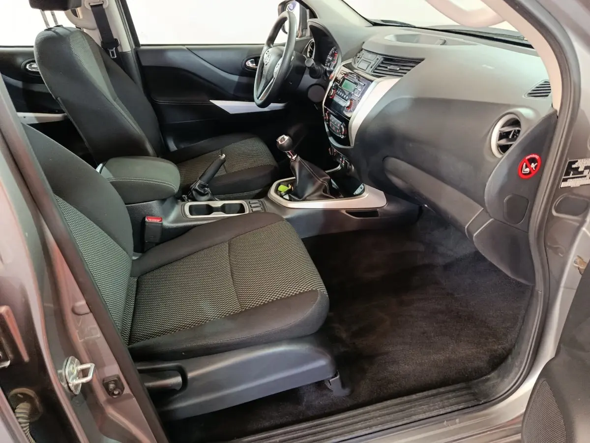 Vue intérieure côté passager avant du Nissan Navara gris clair 2018, montrant sièges noirs et tableau de bord avec boîte manuelle.