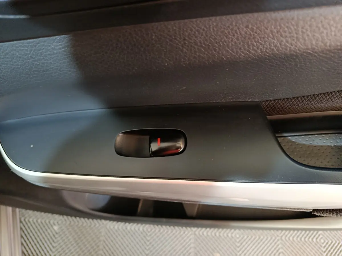 Gros plan sur le bouton de verrouillage de porte noir dans l'habitacle du Nissan Navara gris clair, côté intérieur.