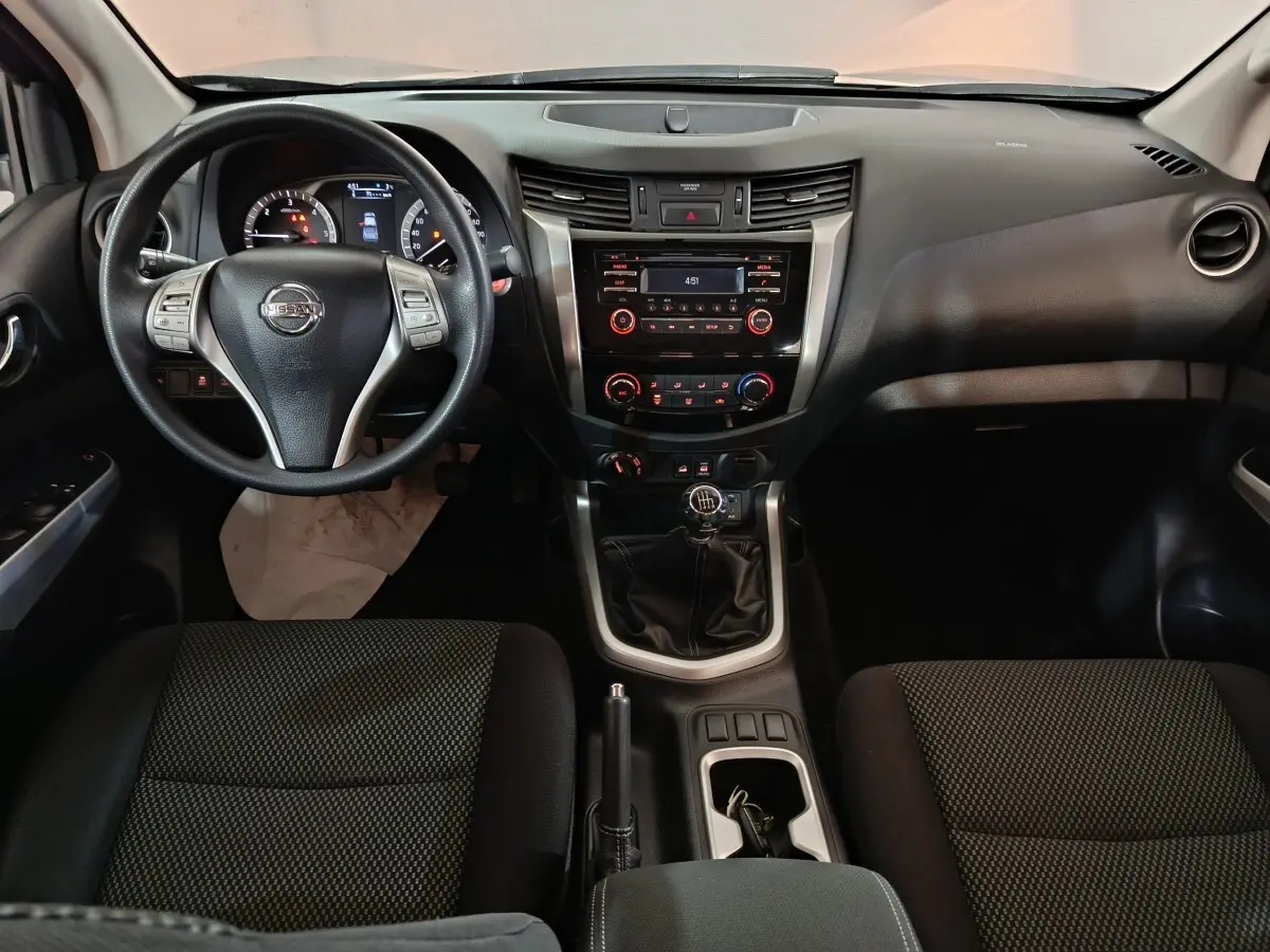 Vue intérieure frontale du tableau de bord du Nissan Navara gris clair, volant multifonctions et levier de vitesse manuel visibles.