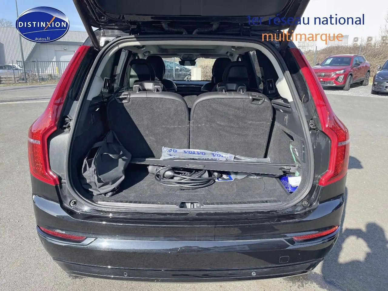 Coffre ouvert vu de l'arrière d'un Volvo XC90 noir avec sièges rabattus et accessoires à l'intérieur.