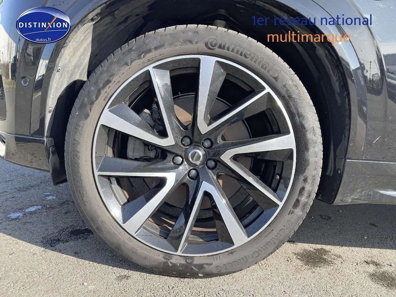 Gros plan sur la roue avant gauche du Volvo XC90 noir, mettant en valeur la jante alu bicolore au design moderne.