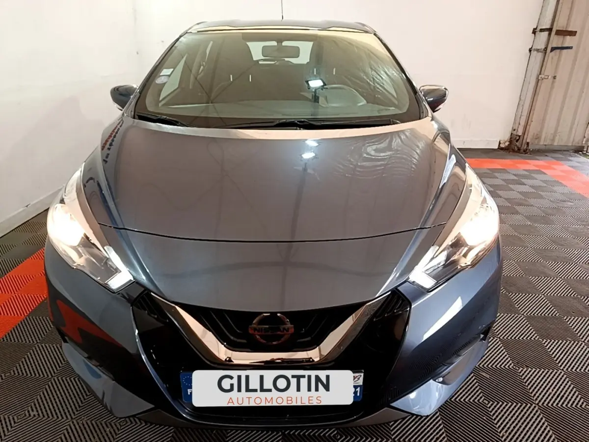 Vue avant d'une Nissan Micra IG-T 100 Business Edition gris foncé avec phares allumés dans un garage.