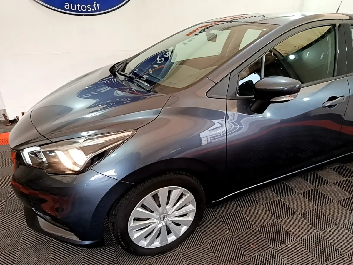 Vue 3/4 avant droit d'une Nissan Micra IG-T 100 Business Edition gris foncé avec phares allumés et jantes argentées.