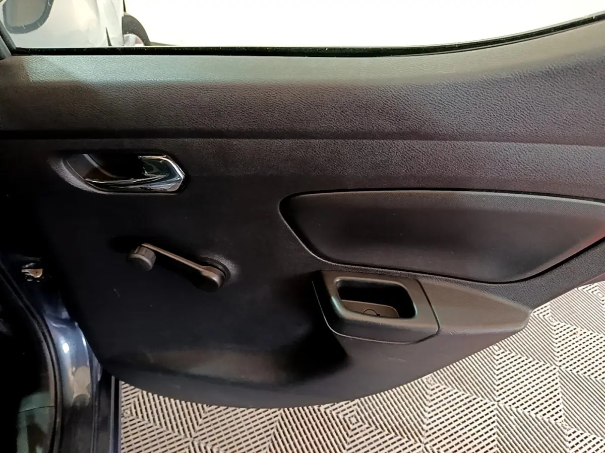 Vue intérieure du panneau de porte côté conducteur d'une Nissan Micra gris foncé, avec poignée chromée et commande manuelle de vitre.