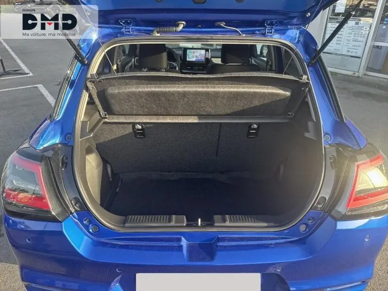 Coffre ouvert vu de l'arrière d'une Suzuki Swift 1.2 Hybrid bleu Frontier Pearl, intérieur noir et écran tactile visible.