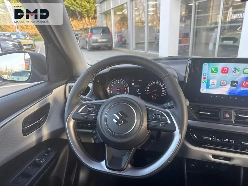 Vue intérieure centrée sur le volant cuir multifonction de la Suzuki Swift 1.2 Hybrid, avec tableau de bord et écran tactile visible.