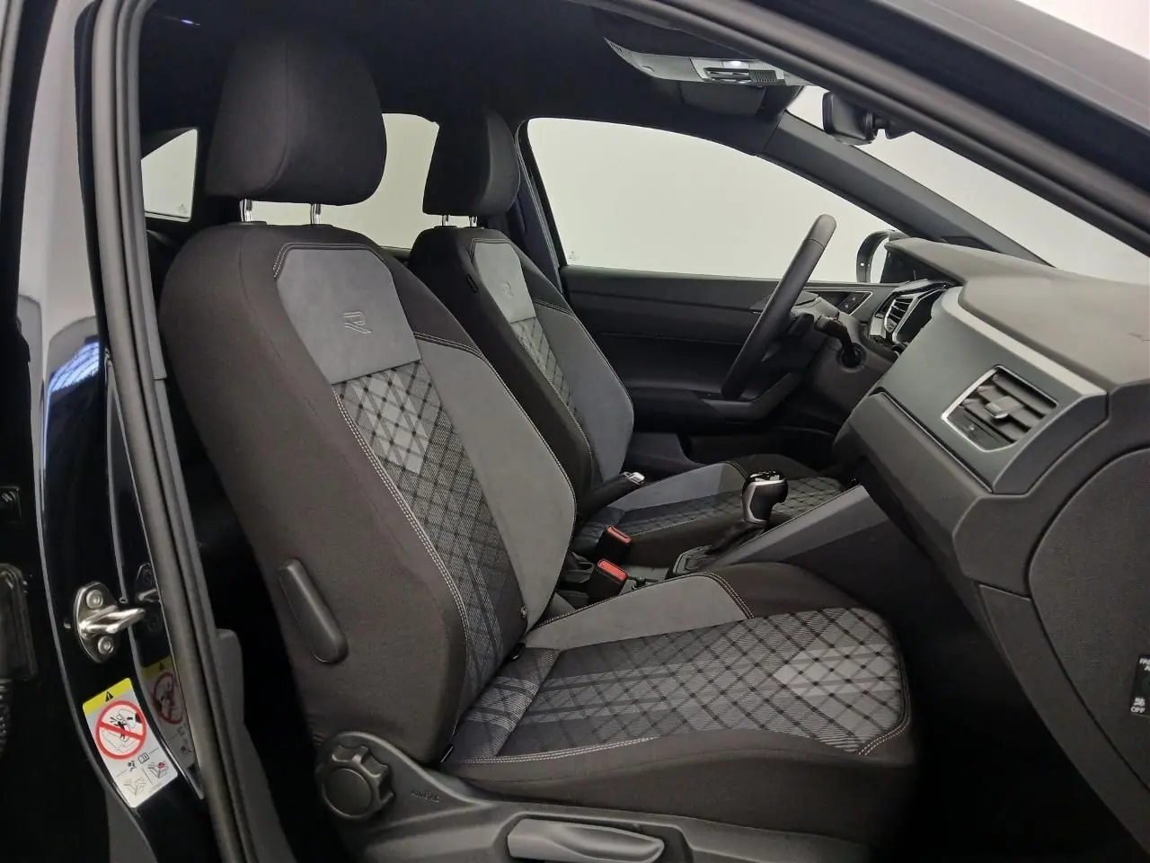 Vue intérieure côté gauche du Volkswagen Taigo 1.5 TSI R-Line 2025, sièges sport noirs avec surpiqûres grises et volant multifonctions.