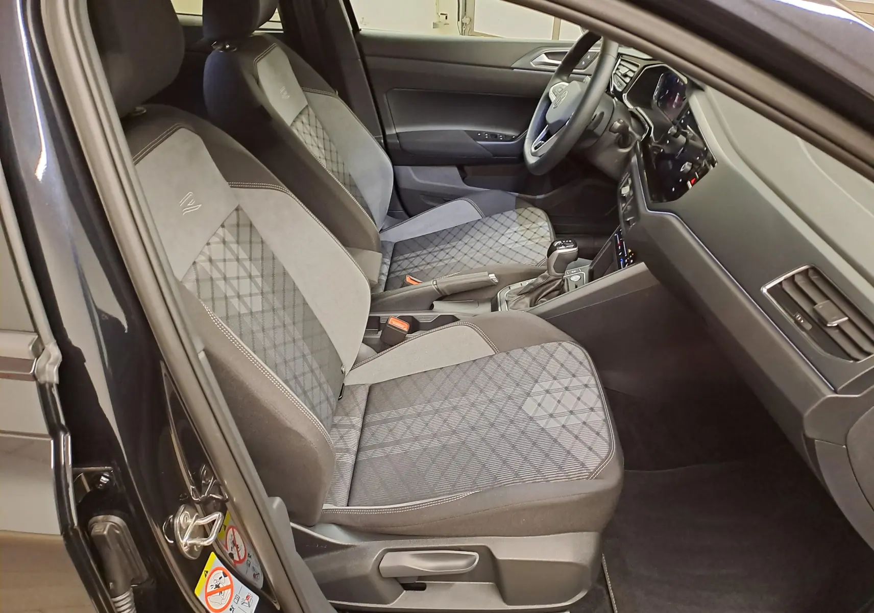 Vue intérieure côté gauche du Volkswagen Taigo noir intense nacré, mettant en valeur les sièges avant sport-confort et la console centrale.