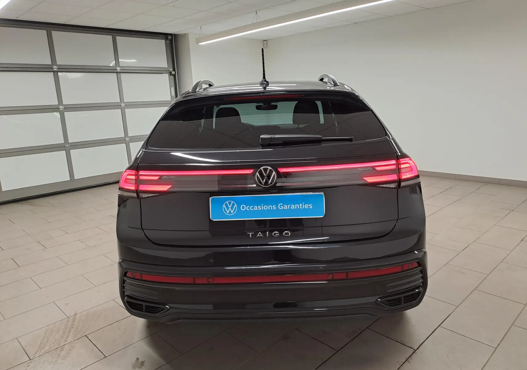 Vue arrière d'un Volkswagen Taigo noir intense nacré avec feux arrière allumés et logo VW visible.