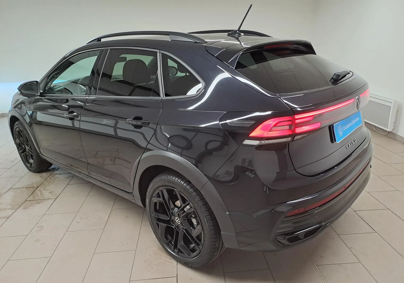 Vue 3/4 arrière droite du Volkswagen Taigo noir intense nacré avec jantes noires et feux arrière LED allumés.