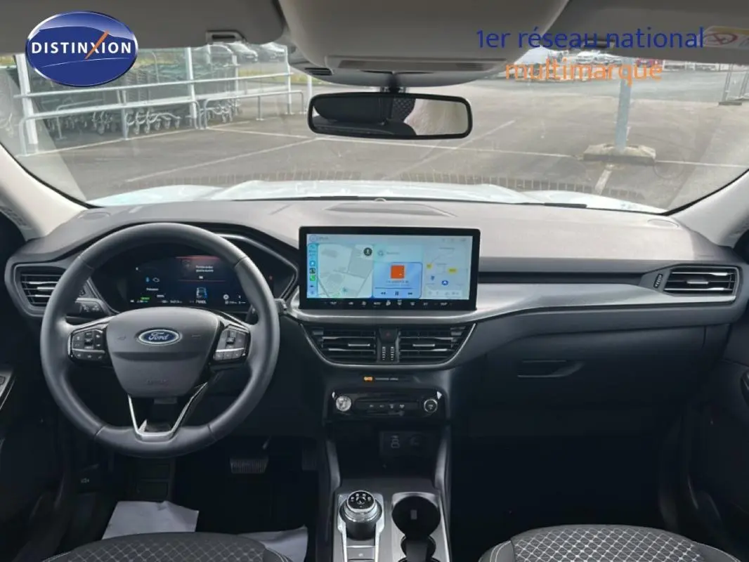 Vue intérieure frontale du tableau de bord noir du Ford Kuga blanc 2025 avec écran tactile central et volant multifonction.