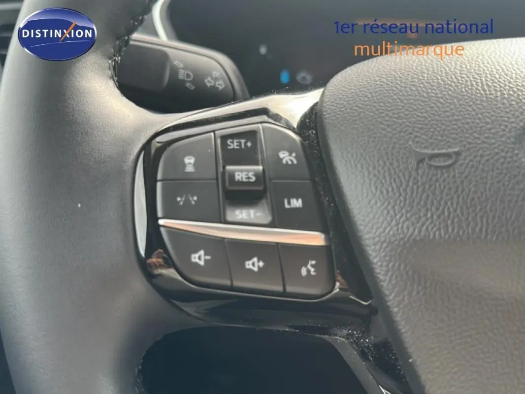 Gros plan sur les commandes au volant côté gauche du Ford Kuga blanc 2025 avec régulateur et limiteur de vitesse.