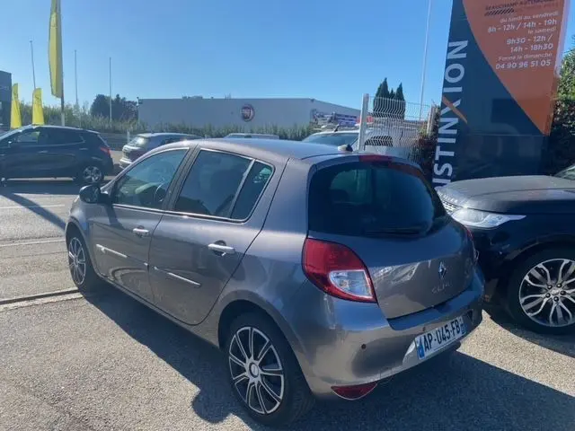 Vue 3/4 arrière droite d'une Renault Clio III 110 ch exception tomtom grise métallisée stationnée en extérieur.