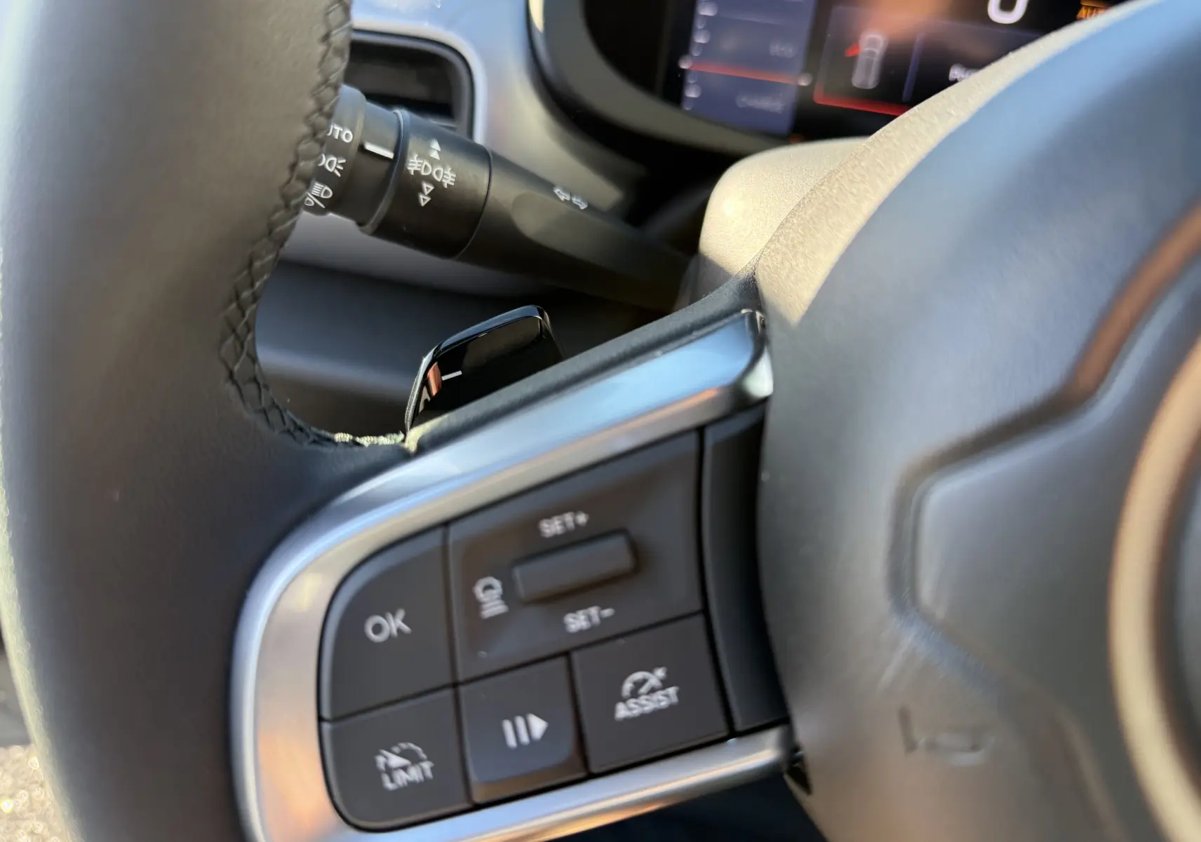 Gros plan sur les commandes au volant côté gauche du Jeep Avenger 2025 gris Storm, avec affichage numérique en arrière-plan.