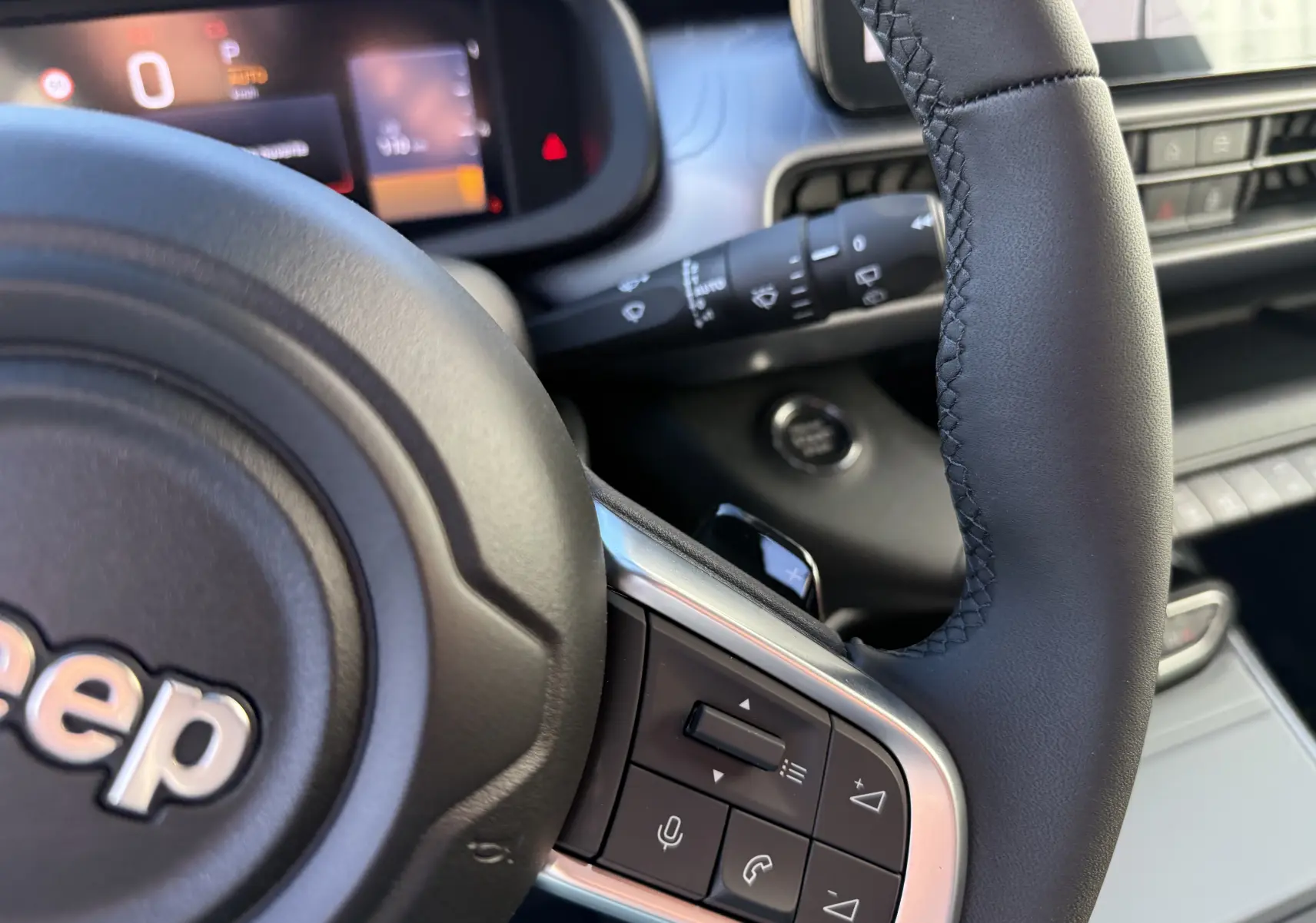 Gros plan sur le volant noir de la Jeep Avenger 2025, montrant les commandes intégrées côté droit et le tableau de bord numérique flou.