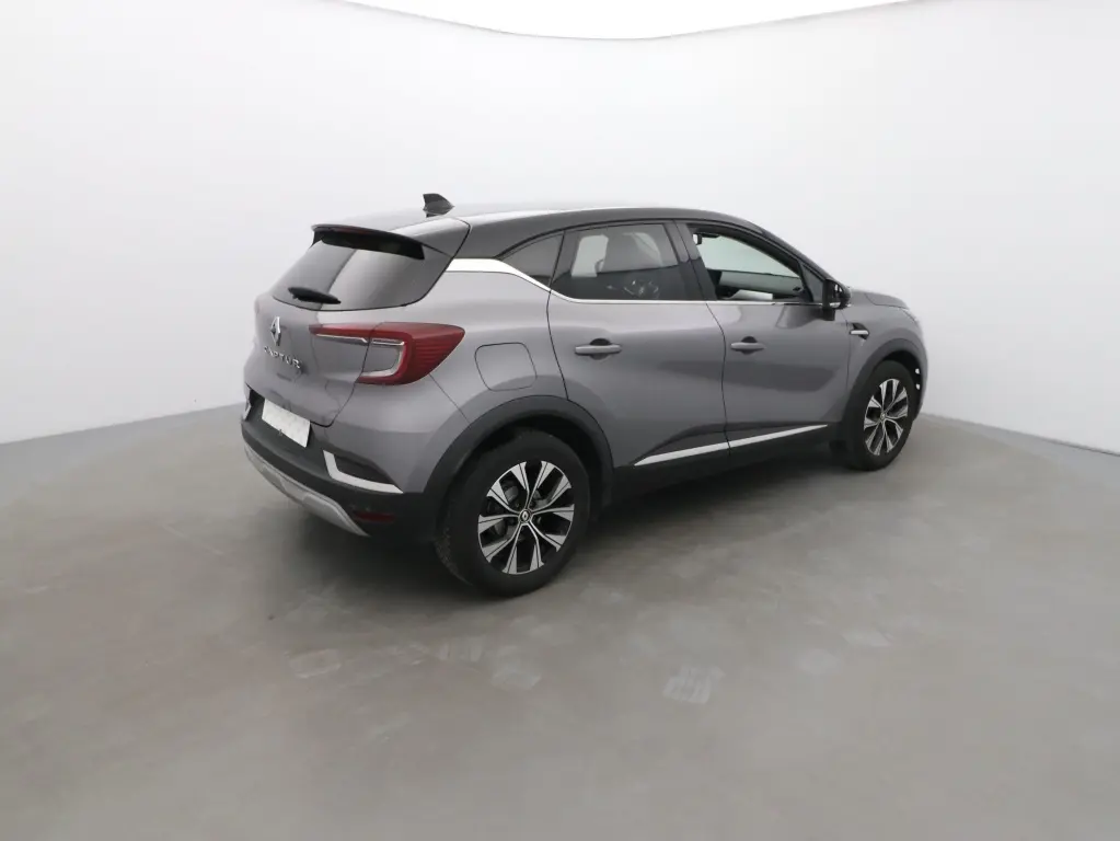 Vue 3/4 arrière droite d'un Renault Captur 2024 gris Cassiopée avec toit noir et jantes alliage bicolores.