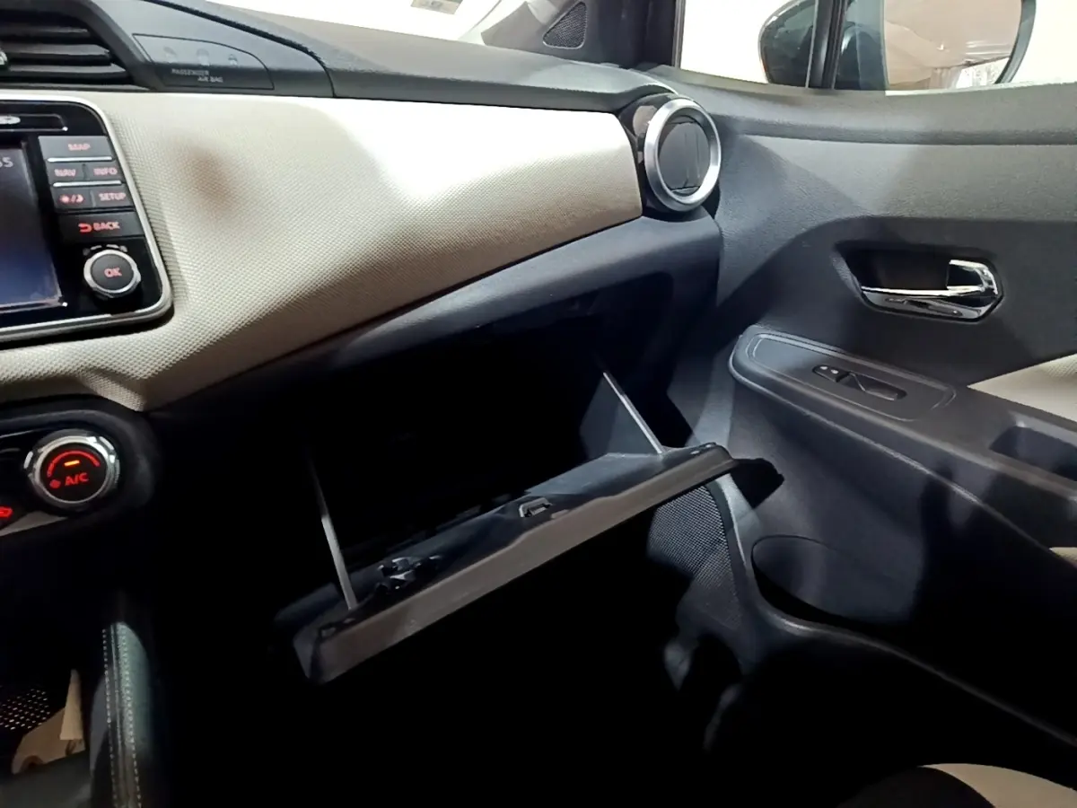 Vue intérieure côté passager de la Nissan Micra noire, boîte à gants ouverte et tableau de bord clair texturé.