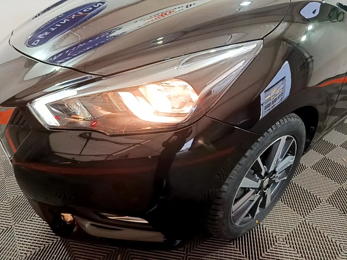 Gros plan sur l'avant droit noir de la Nissan Micra IG-T 90 N-Connecta avec phare allumé et jante alliage visible.