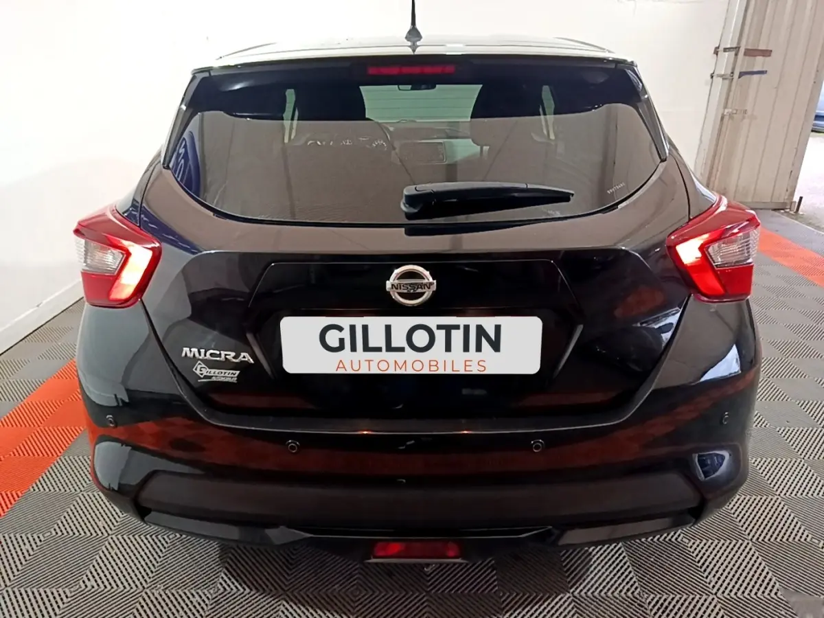 Vue arrière d'une Nissan Micra noire 2017 avec feux arrière allumés et logo visible sur un sol à damier rouge et gris.