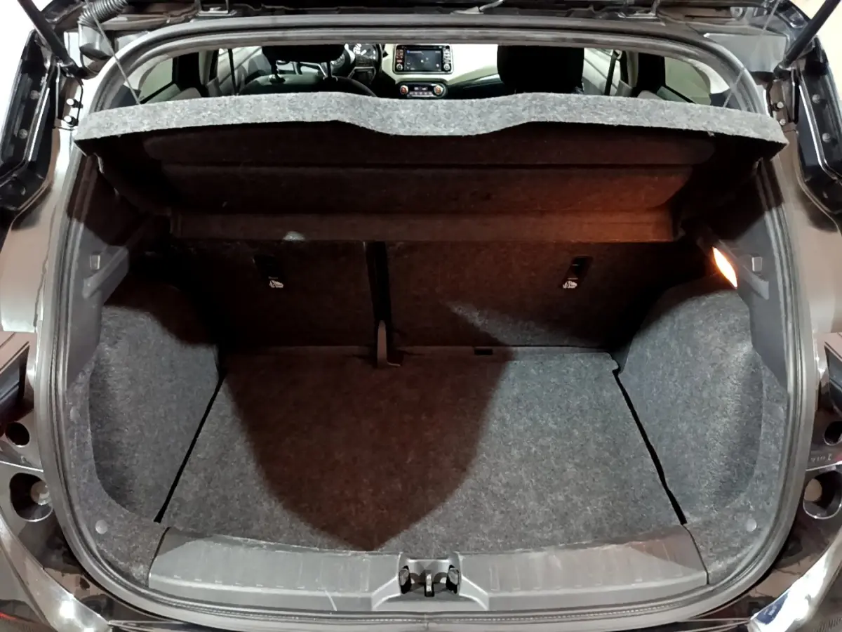 Coffre ouvert vu de l'arrière d'une Nissan Micra noire, intérieur du coffre en tissu gris avec tablette relevée.