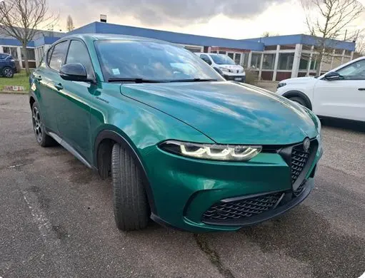 Alfa Romeo Tonale vert foncé vue 3/4 avant gauche, phares LED allumés, sur parking extérieur.