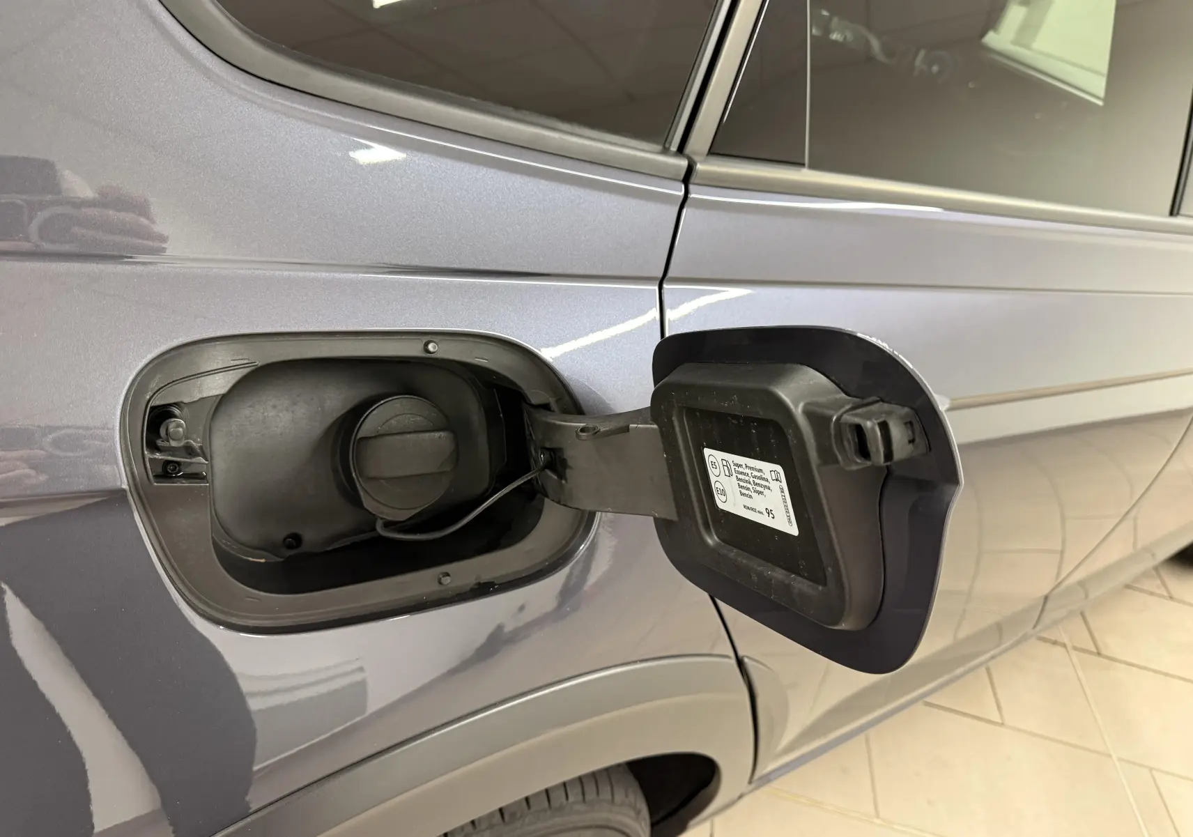 Vue latérale gauche du Volkswagen Taigo gris cendre, avec trappe à carburant essence ouverte et bouchon visible.