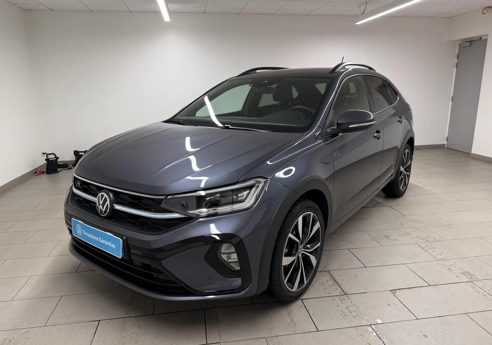 Volkswagen Taigo gris cendre en 3/4 avant droit, avec jantes alliage 18'' et calandre R-Line visible.