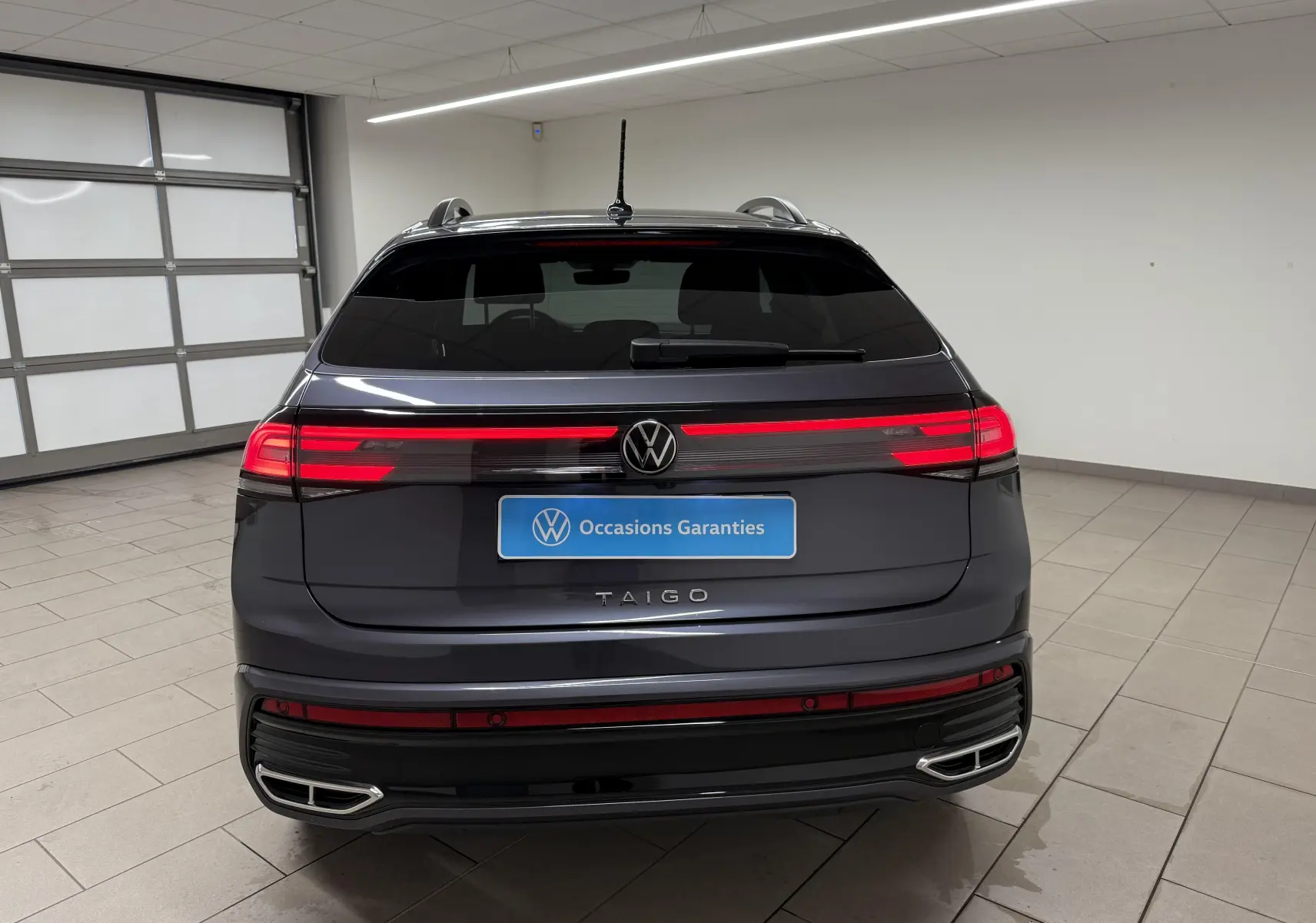 Vue arrière du Volkswagen Taigo gris cendre avec feux LED allumés et double sortie d'échappement intégrée au pare-chocs.