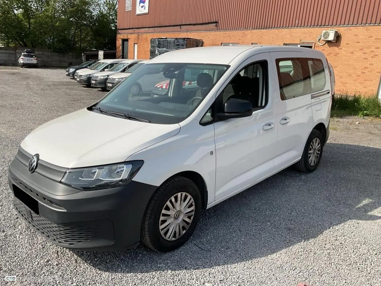 Volkswagen Caddy blanc Candy vue 3/4 avant droit, avec pare-chocs noir et portes coulissantes visibles.