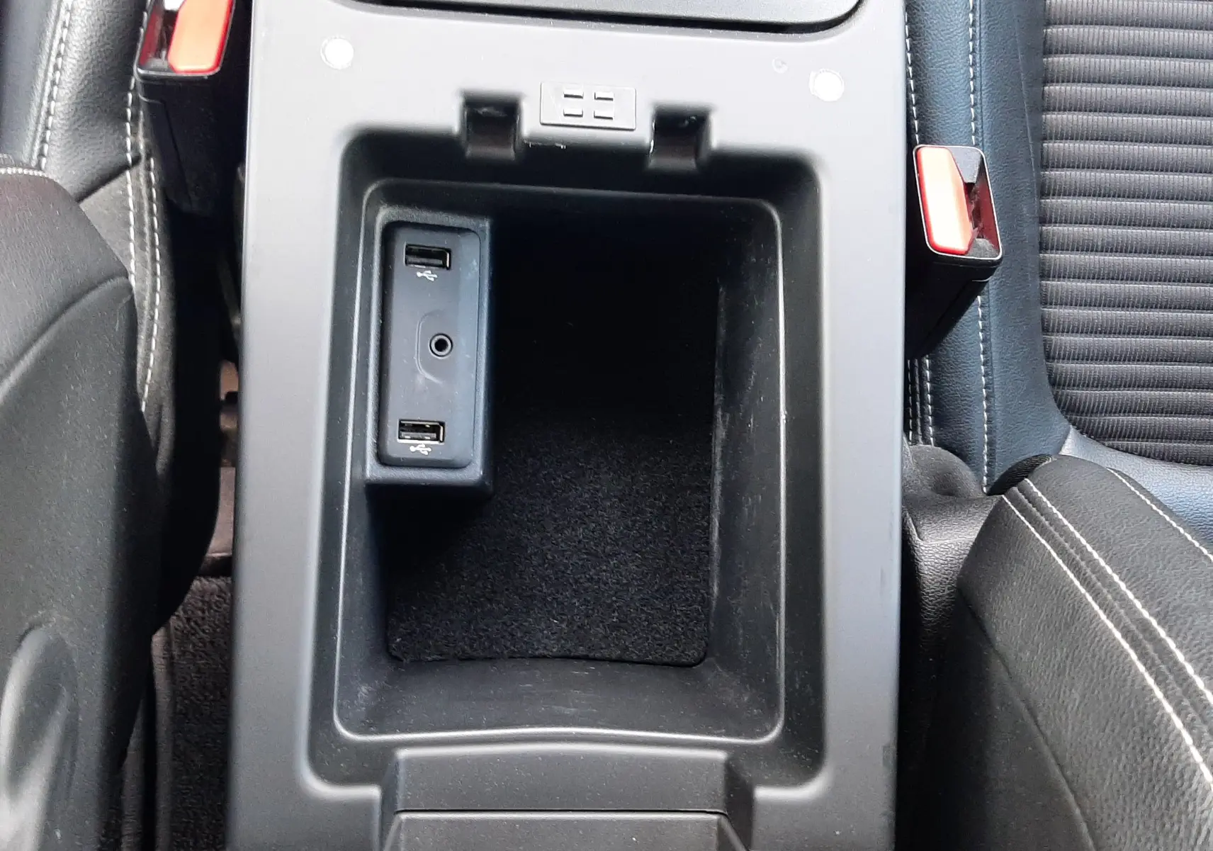 Vue plongeante sur l'accoudoir central en cuir noir entre les sièges avant en tissu et cuir du Renault Scénic IV.