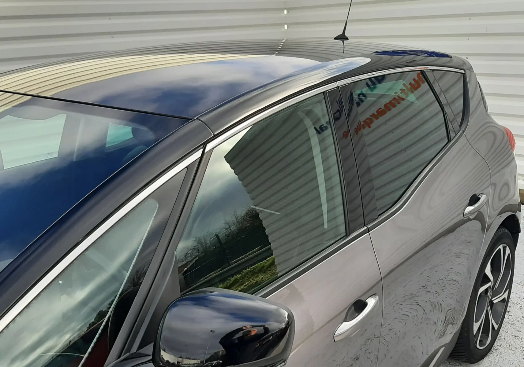 Vue de côté droit avant d'un Renault Scénic IV gris Cassiopée avec toit et rétroviseur noir brillant.