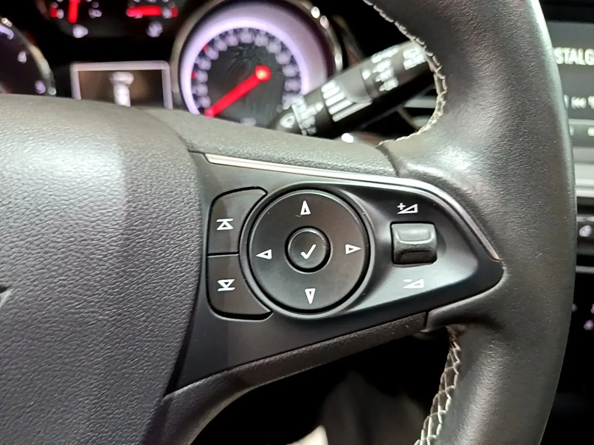 Gros plan sur les commandes multifonctions noires du volant cuir de l’Opel Insignia 2019, tableau de bord en arrière-plan.