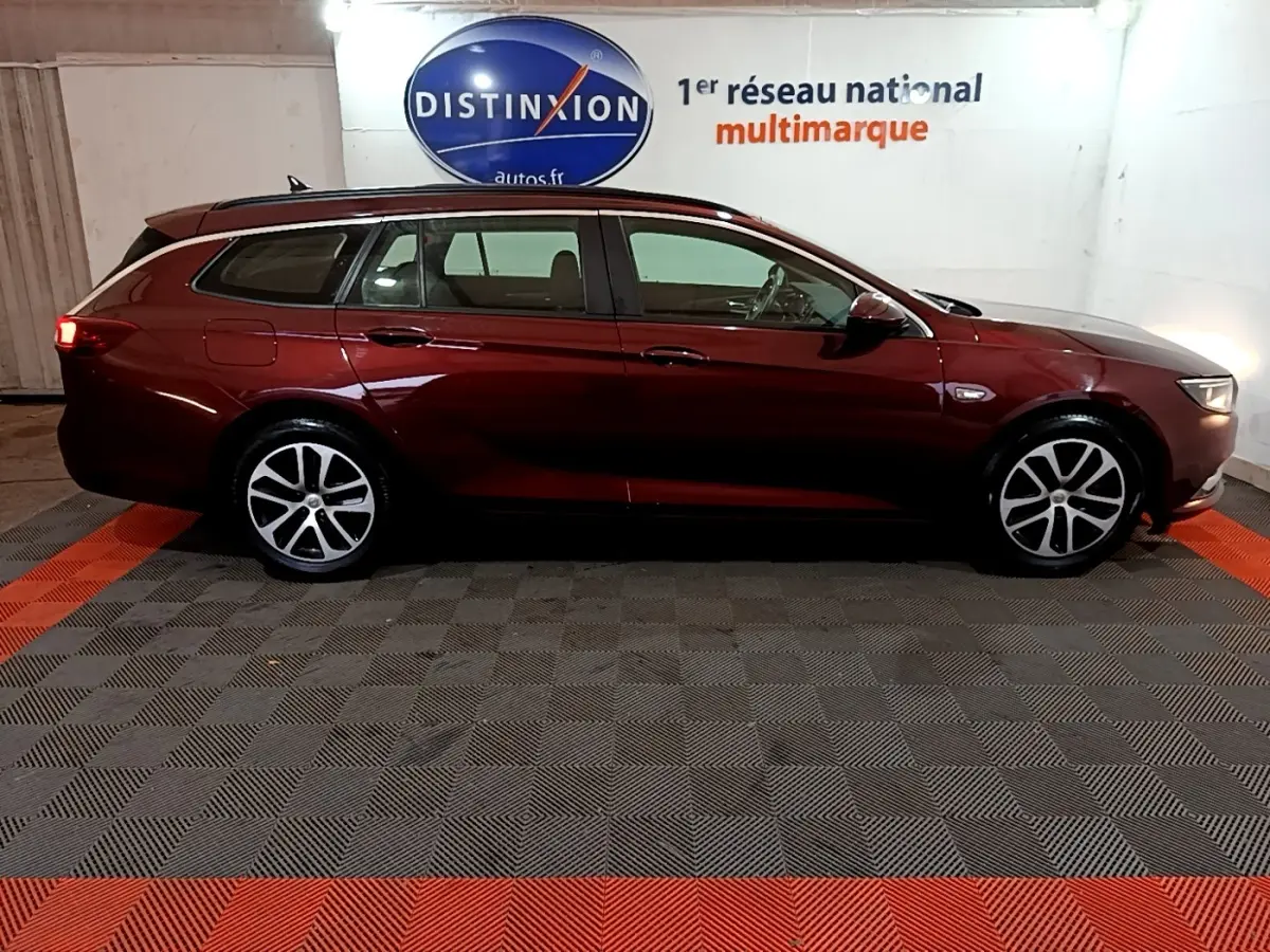 Vue latérale droite d'une Opel Insignia break rouge 2019 dans un showroom avec sol à damier gris et rouge.