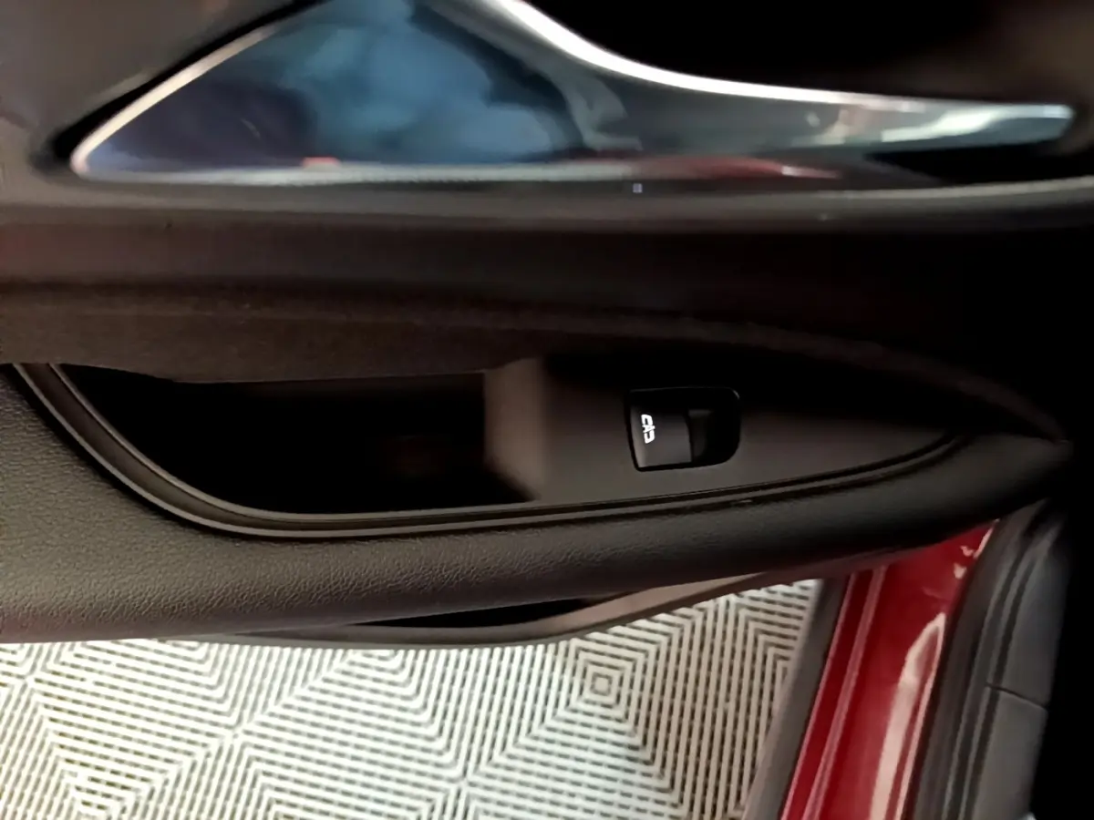 Gros plan sur la poignée intérieure et bouton de verrouillage de la porte côté conducteur d’une Opel Insignia rouge.