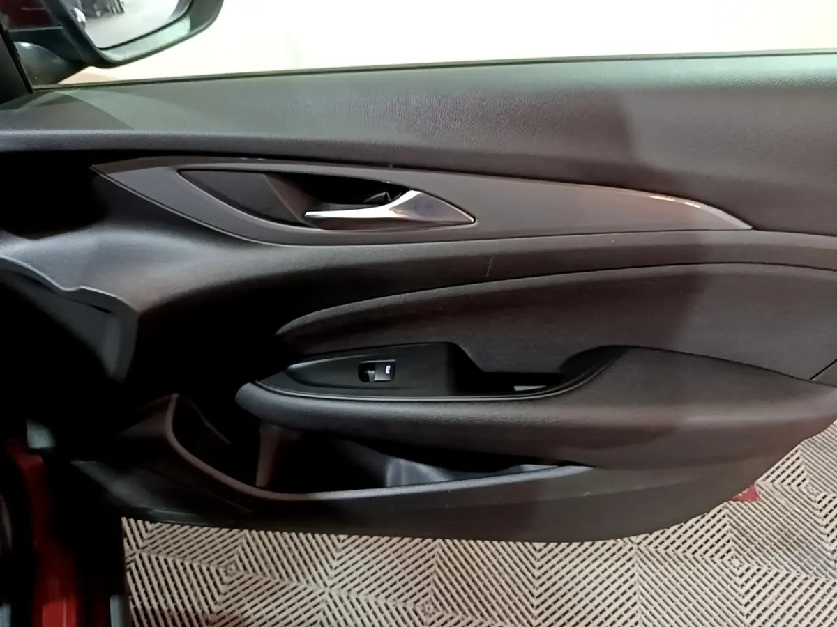 Vue rapprochée de la porte côté conducteur de l’Opel Insignia rouge, avec poignée argentée et commande de vitre.