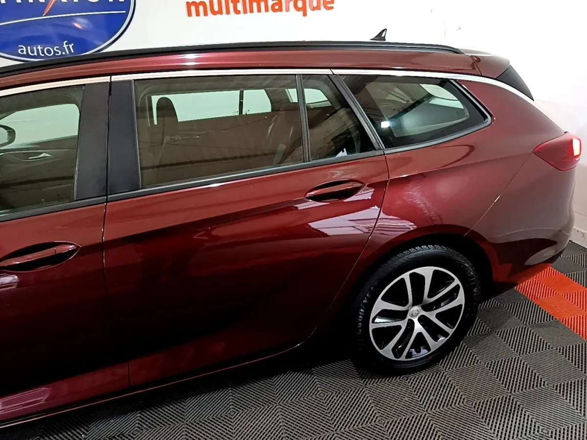 Vue latérale côté droit d'une Opel Insignia break rouge métallisé, mettant en valeur les jantes alliage et la ligne fluide du toit.