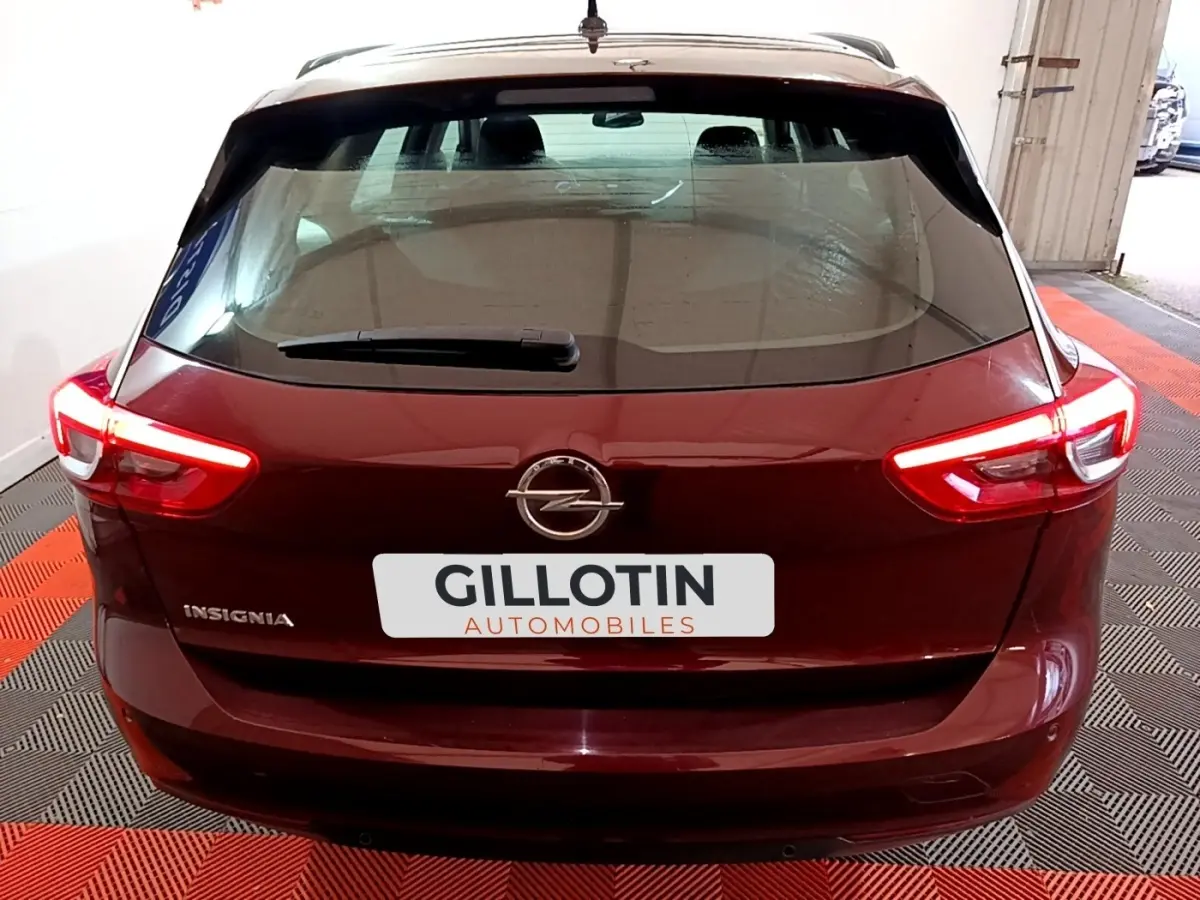 Vue arrière d'une Opel Insignia rouge avec feux arrière allumés dans un garage au sol rouge et noir.