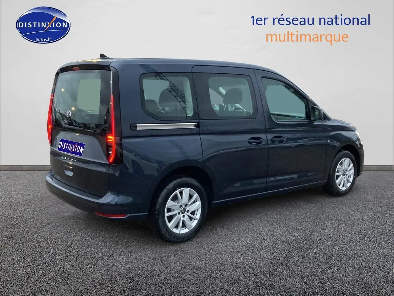 Volkswagen Caddy bleu métallisé vu de profil droit, avec feux arrière verticaux allumés et jantes argentées.