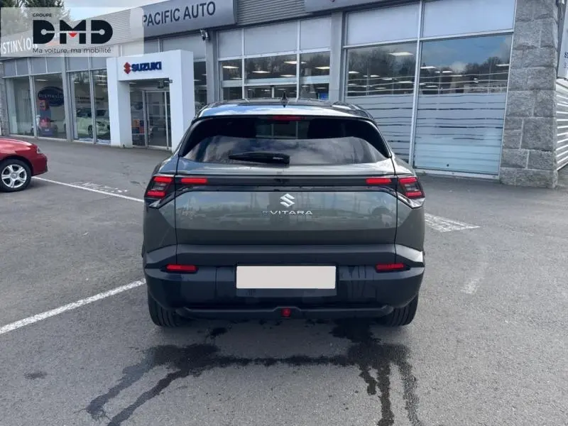 Vue arrière du Suzuki Vitara électrique 2026 en vert Land Breeze avec toit noir, stationné devant un concessionnaire.