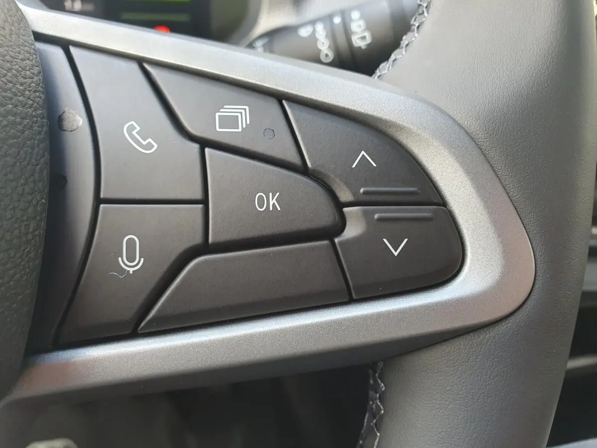 Gros plan sur les commandes multifonctions noires du volant du Dacia Dokker Van gris schiste, avec boutons de navigation et appel.