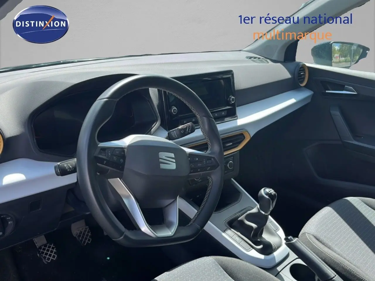 Vue intérieure du poste de conduite de la SEAT Arona bleu Fjord, volant multifonction et levier de vitesse manuel visibles.