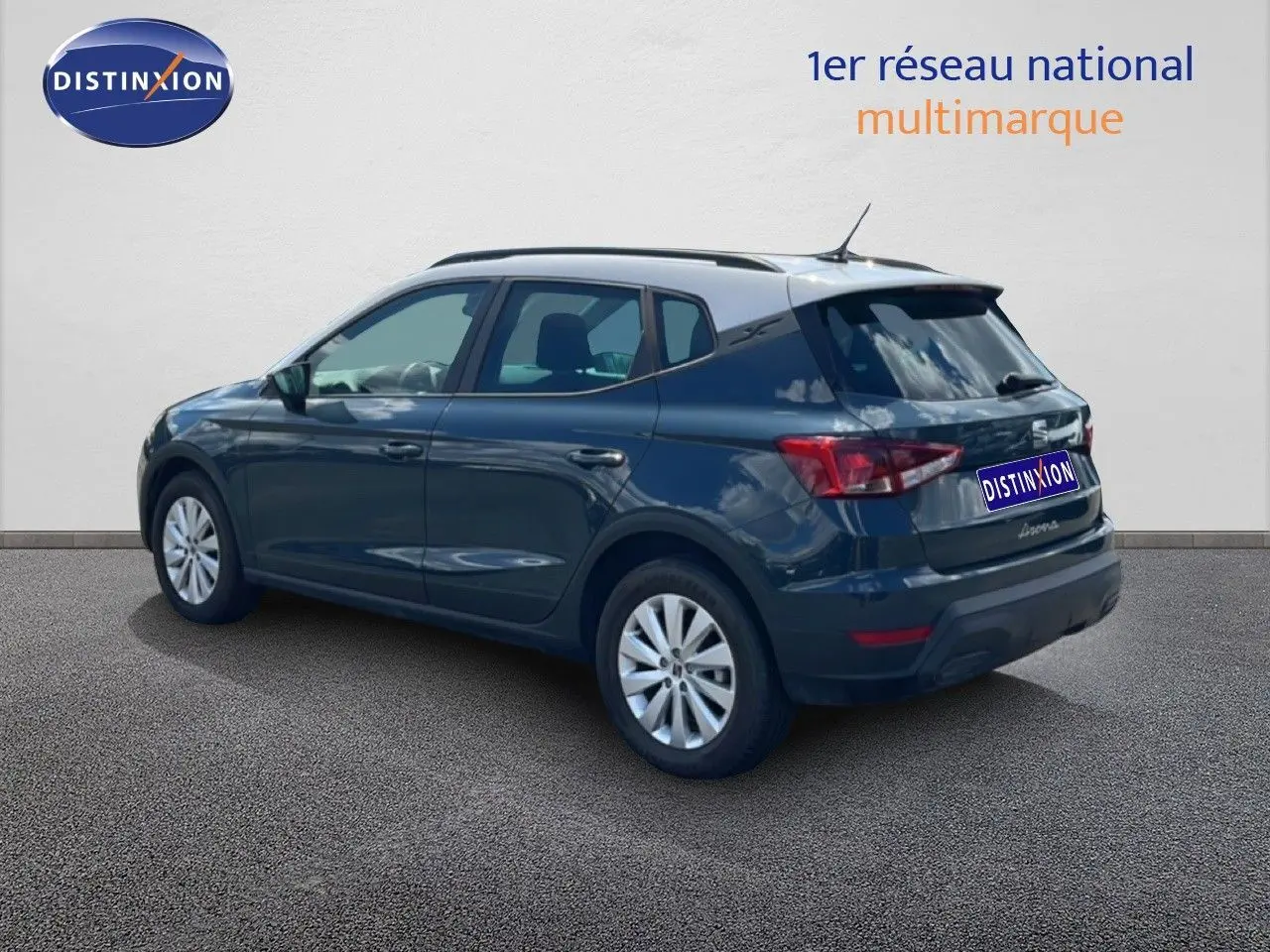 Vue 3/4 arrière droite d'une SEAT Arona bleu Fjord avec toit blanc, stationnée sur sol gris devant un mur clair.
