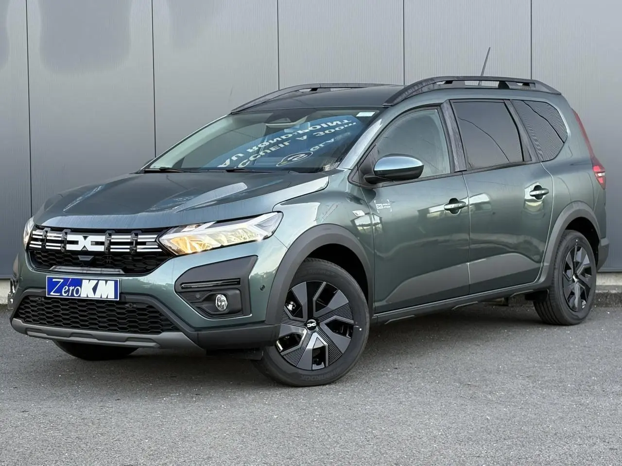 Vue 3/4 avant droit du Dacia Jogger 2024 Vert Cèdre avec barres de toit et jantes noires distinctives.