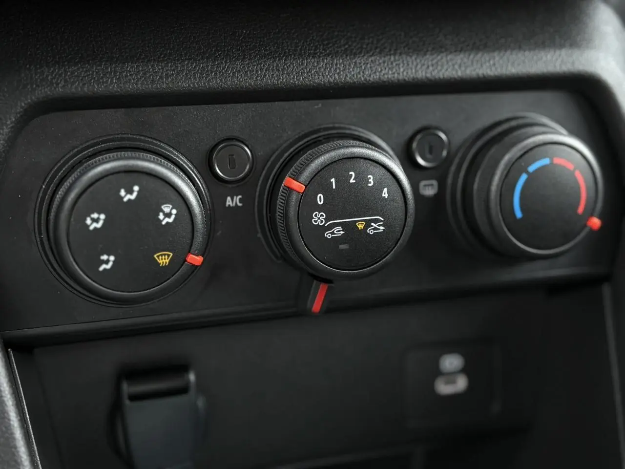 Gros plan sur les commandes de climatisation manuelle du Dacia Jogger 2024, boutons noirs avec indicateurs rouges et bleus.