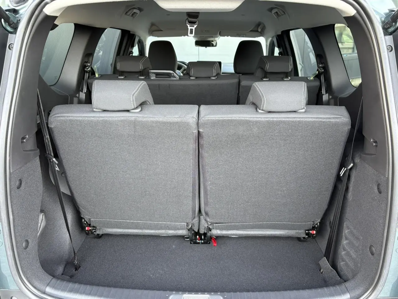 Vue arrière du coffre du Dacia Jogger Vert Cèdre 2024 avec sièges du troisième rang rabattus et tissu gris.
