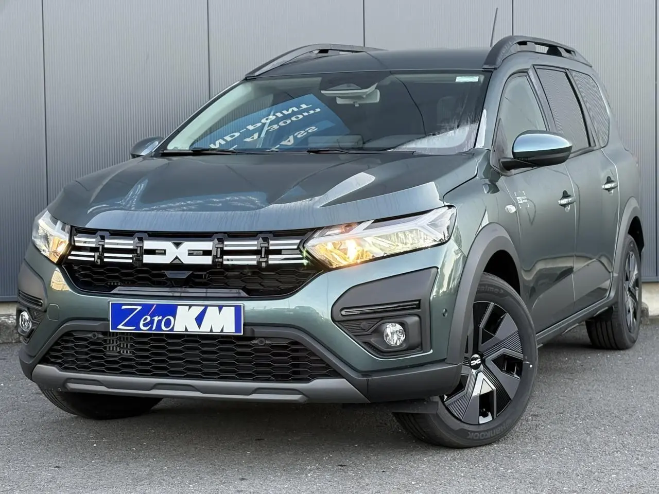 Vue 3/4 avant droite du Dacia Jogger Vert Cèdre 2024 avec signature lumineuse LED et barres de toit longitudinales.