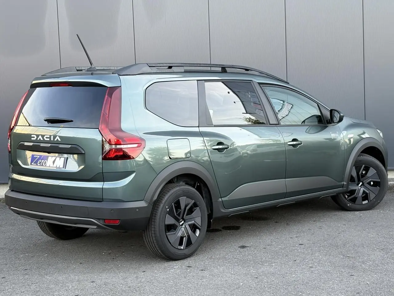 Vue 3/4 arrière droite d'un Dacia Jogger Vert Cèdre avec barres de toit et jantes noires modernes.