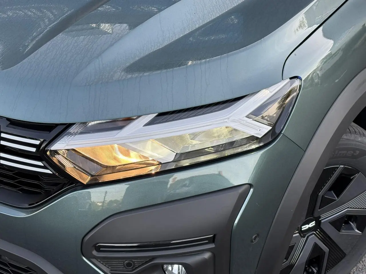 Gros plan sur le phare avant droit et la calandre du Dacia Jogger 2024 en Vert Cèdre avec jante noire distinctive.