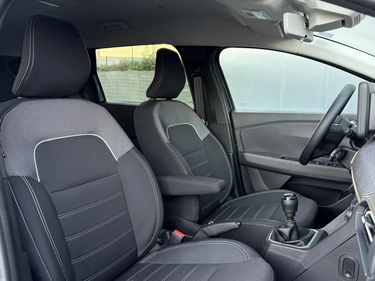 Vue intérieure côté conducteur du Dacia Jogger 2024, sièges tissu noirs avec surpiqûres blanches et boîte manuelle.